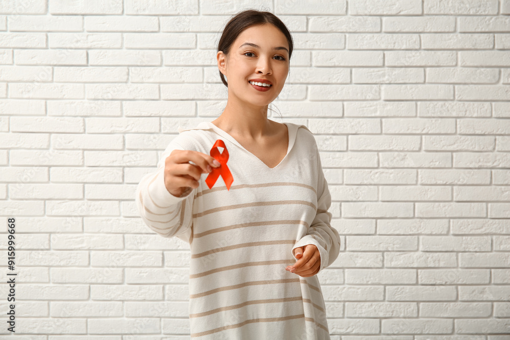 Pretty young woman with red ribbon near white brick wall. World AIDS Day concept Pretty young woman with red ribbon near white brick wall. World AIDS Day concept