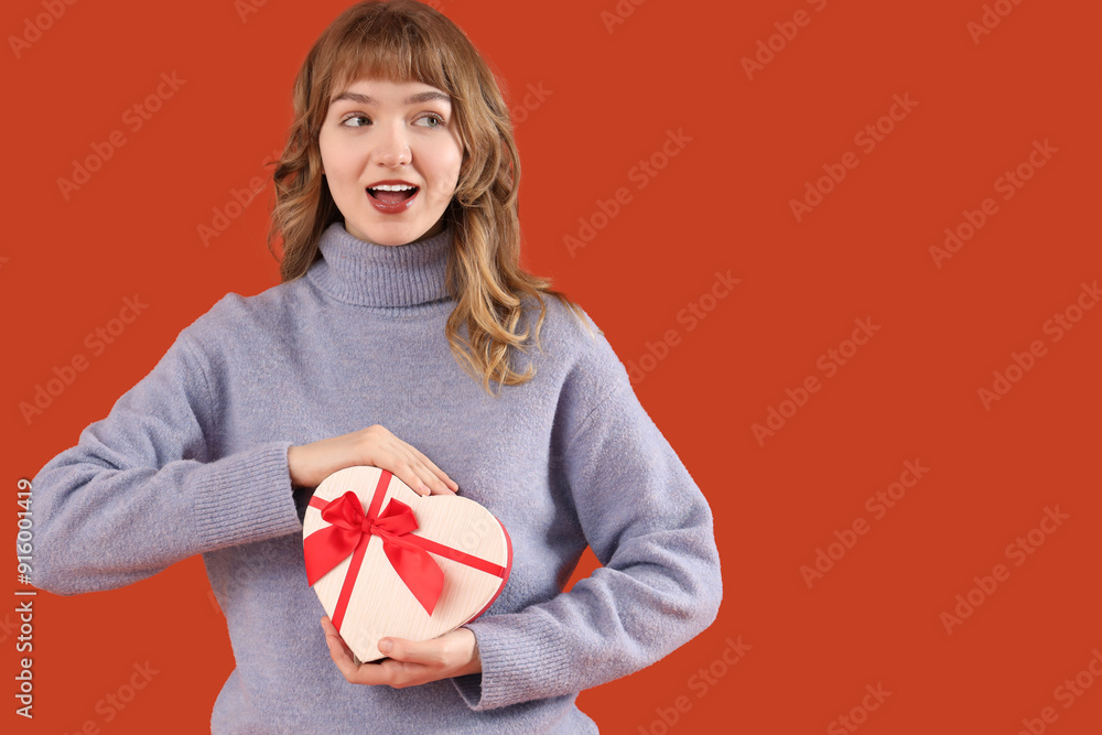 Beautiful young shocked woman with gift box for Valentine's Day on orange background Beautiful young shocked woman with gift box for Valentine's Day on orange background