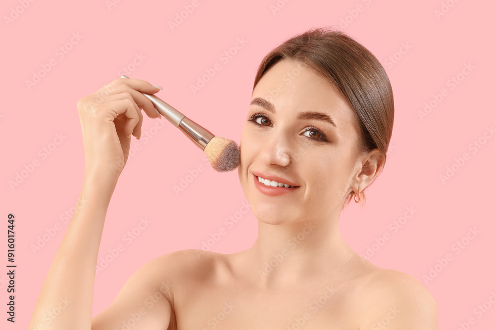 Fototapeta premium Beautiful young woman with makeup brush on pink background