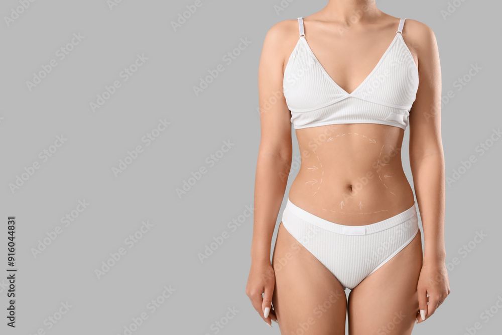 Young woman in underwear with marks on her belly against grey background. Plastic surgery concept Young woman in underwear with marks on her belly against grey background. Plastic surgery concept
