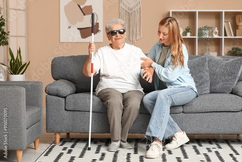 Foto Young woman helping her blind grandmother to stand up from sofa at home