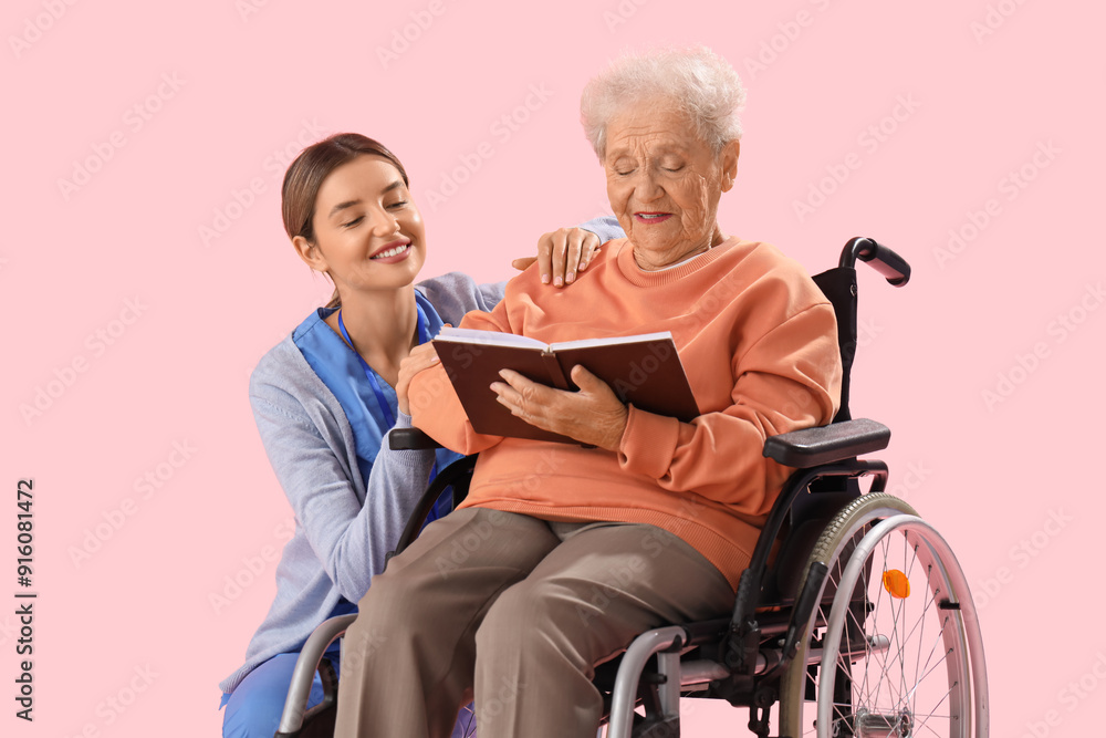 Senior woman in wheelchair with nurse reading book on pink background Senior woman in wheelchair with nurse reading book on pink background