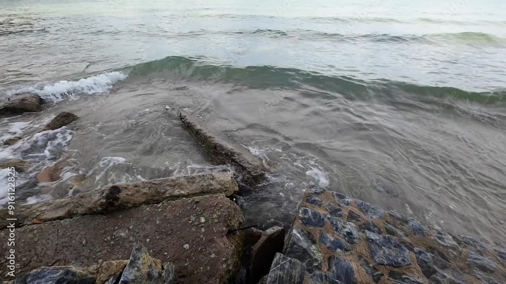 Calm waves gently lap against the rocky shore at a tranquil beach in the early morning Calm waves gently lap against the rocky shore at a tranquil beach in the early morning