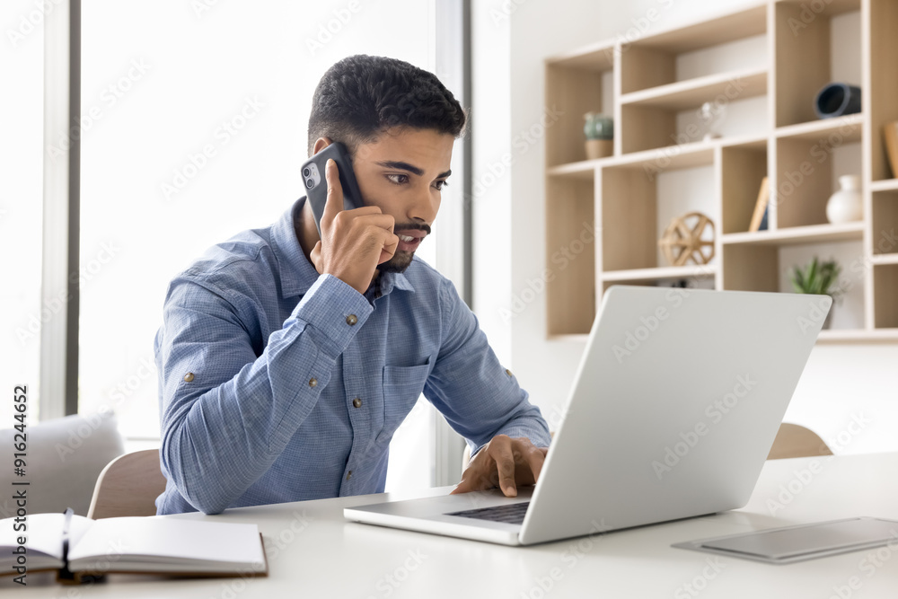 Serious young Arab business man talking on cellphone, work app, client online service on laptop, Internet technology for job telephone conversation, typing, giving consultation Serious young Arab business man talking on cellphone, work app, client online service on laptop, Internet technology for job telephone conversation, typing, giving consultation