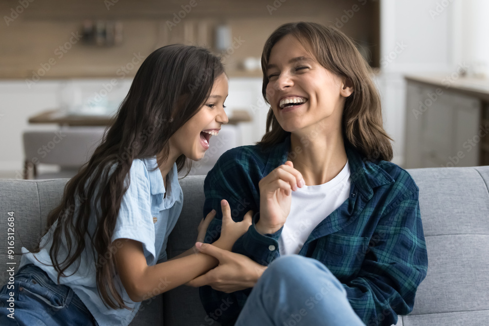 Excited active kid tickling cheerful laughing young mom on sofa, enjoying playtime, leisure, childhood. Mother and daughter girl playing funny game at home together, having fun Excited active kid tickling cheerful laughing young mom on sofa, enjoying playtime, leisure, childhood. Mother and daughter girl playing funny game at home together, having fun