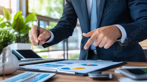 A business professional giving a presentation to colleagues, pointing at charts and graphs on a flipchart in a modern office setting.