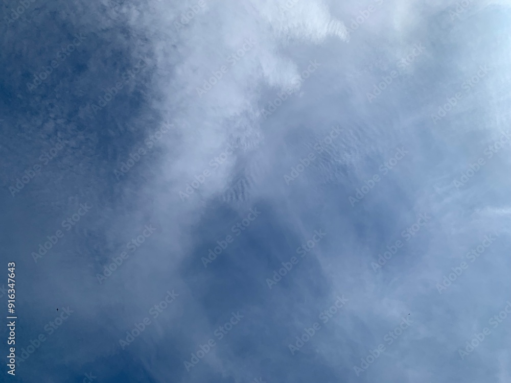 An image of a sky with thinly scattered white clouds and bright light.