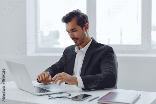 Man in office businessman sitting at desk and working in laptop and talking on phone, modern suit, finance and startup concept and data analysis, working lifestyle in bright office.