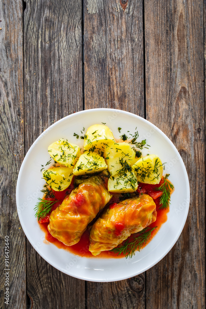 Wrapped minced meat in cabbage leaves served in tomato sauce with boiled potatoes on white plate on wooden table - polish dish gołąbki. Top view
Wrapped minced meat in cabbage leaves served in tomato sauce with boiled potatoes on white plate on wooden table - polish dish gołąbki. Top view