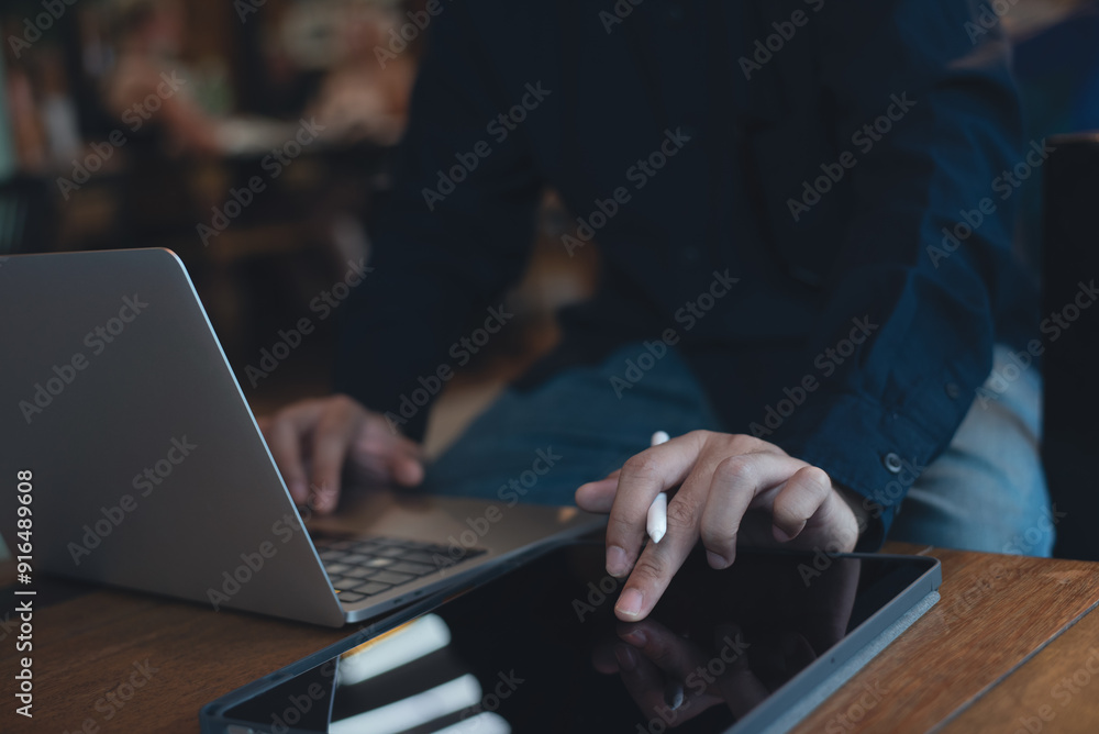 Man working on laptop computer and using digital tablet surfing the internet on wooden table at coffee shop Man working on laptop computer and using digital tablet surfing the internet on wooden table at coffee shop