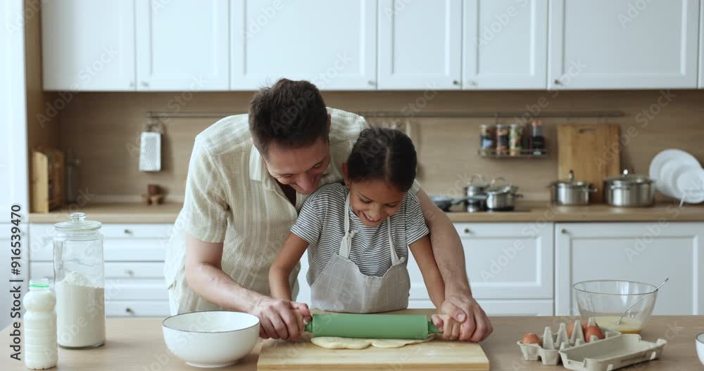 Happy baker dad and adorable daughter kid in apron baking together, rolling dough in home kitchen table, touching faces of each other with floury fingers, having fun, laughing Happy baker dad and adorable daughter kid in apron baking together, rolling dough in home kitchen table, touching faces of each other with floury fingers, having fun, laughing