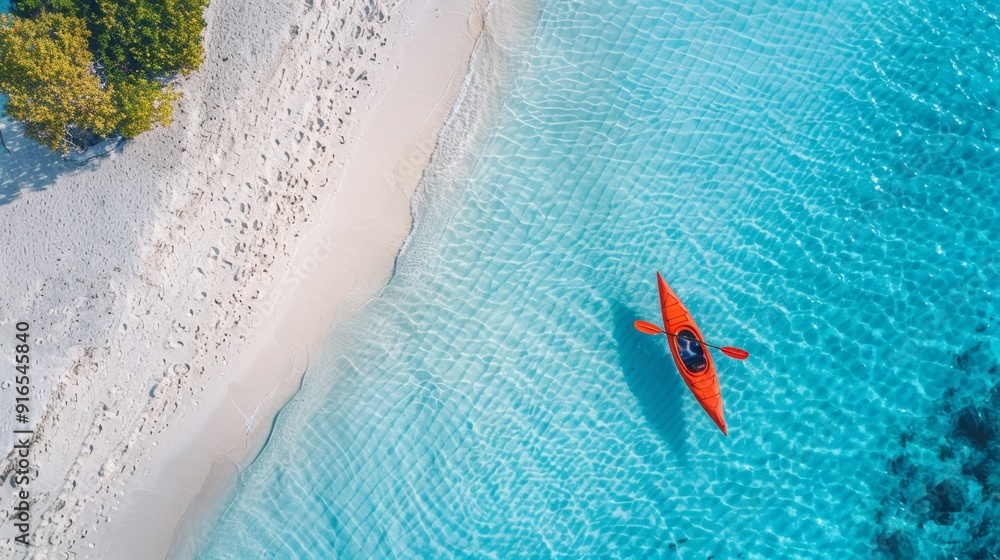 Obraz premium A serene aerial view of a kayak gliding through crystal-clear turquoise water near a sandy beach, capturing the essence of tranquility.