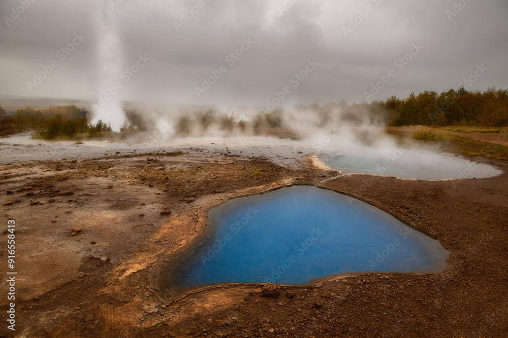 Geothermal dark blue pond at Strokkur Geysir in Iceland, geysir erupting in the background Geothermal dark blue pond at Strokkur Geysir in Iceland, geysir erupting in the background