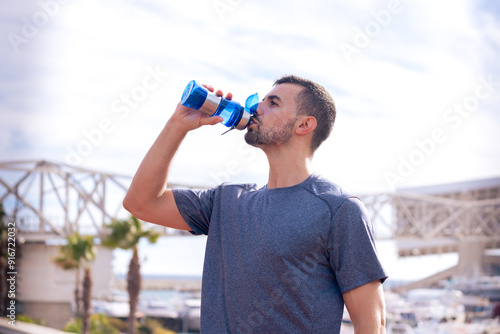 Runner man drinking water from a sports bottle outdoors.