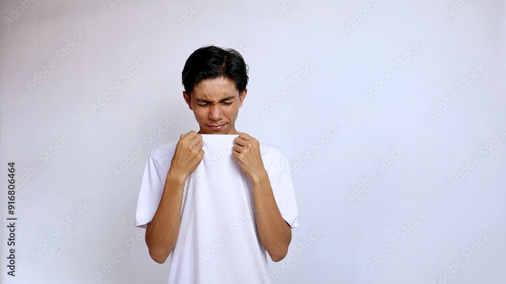 Young Asian man wearing white shirt gesture smelling bad smell from his shirt isolated white background Young Asian man wearing white shirt gesture smelling bad smell from his shirt isolated white background