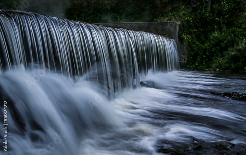 Wonderful lines of water like steel rods flowing over a weir on the Lower Clydach river in South Wales UK