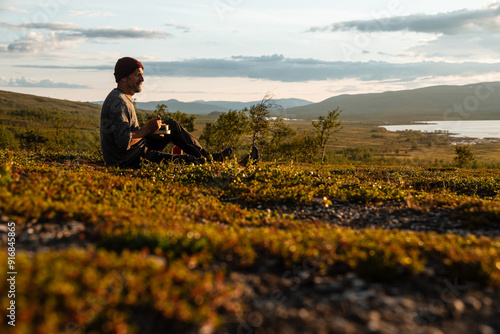 Young white man eating a delicious meal, enjoying the view over Padjelanta National Park in Swedish Lapland during golden hour. Close to Padjelantaleden Kisuris. photo