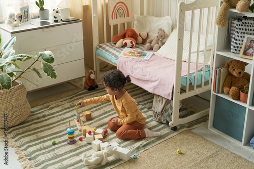 Young child playing with colorful blocks on carpeted floor in cozy bedroom filled with toys and stuffed animals, near crib and dresser photo