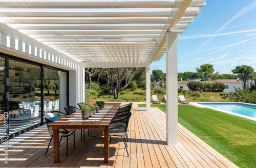 A modern wooden terrace with white slats, surrounded by green grass and an outdoor dining area for several people near the pool