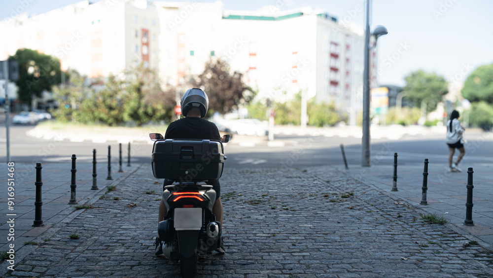 Obraz premium A man on a motorcycle is riding down a street with a building in the background