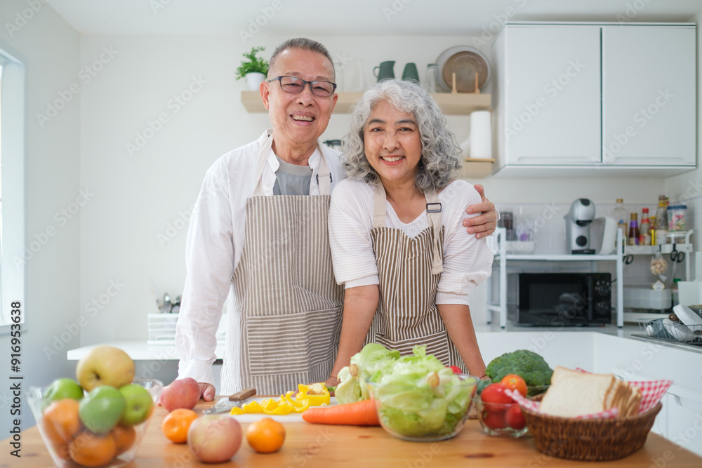 Happy elderly couple wearing aprons standing in the kitchen and smiling warmly at the xcamera. Healthy lifestyle and retirement lifestyle concept. Happy elderly couple wearing aprons standing in the kitchen and smiling warmly at the xcamera. Healthy lifestyle and retirement lifestyle concept.