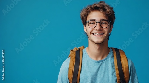 Smart smiling university student with braces on teeth holding backpack looking at camera isolated on blue background Education concept copy space : Generative AI photo