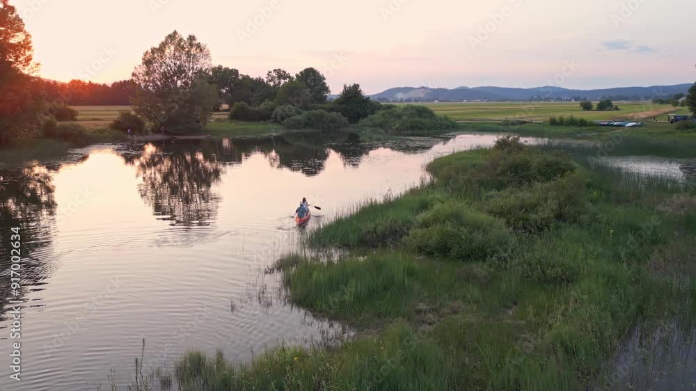 Canoe tandem paddling in the serene lake enjoying the majestic natural surroundings and dusk rays, aerial shot. Peace and quiet concept.