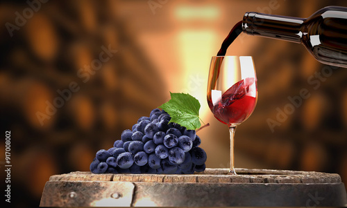 Vin rouge versé d'une bouteille dans un verre à vin. Grappe de raisin noir posé sur un tonneau de vin dans une cave. Appel à la dégustation.