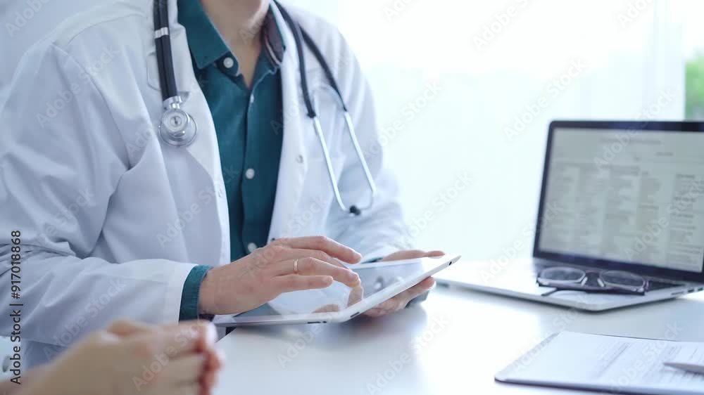Doctor and a patient. The physician, wearing a white medical coat over a green shirt, is using tablet computer during a consultation in the clinic. Medicine concept Doctor and a patient. The physician, wearing a white medical coat over a green shirt, is using tablet computer during a consultation in the clinic. Medicine concept