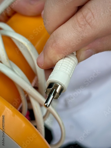 Close-Up of a Hand Holding a Vintage Electrical Plug Connected to a Tangled White Cord, Orange Background