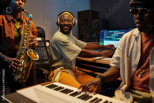 Musicians performing in professional recording studio environment with various audio equipment surrounding recording engineer focused on mixing tracks photo