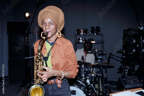 Fototapeta Portrait of young musician playing saxophone during band rehearsal in music stud