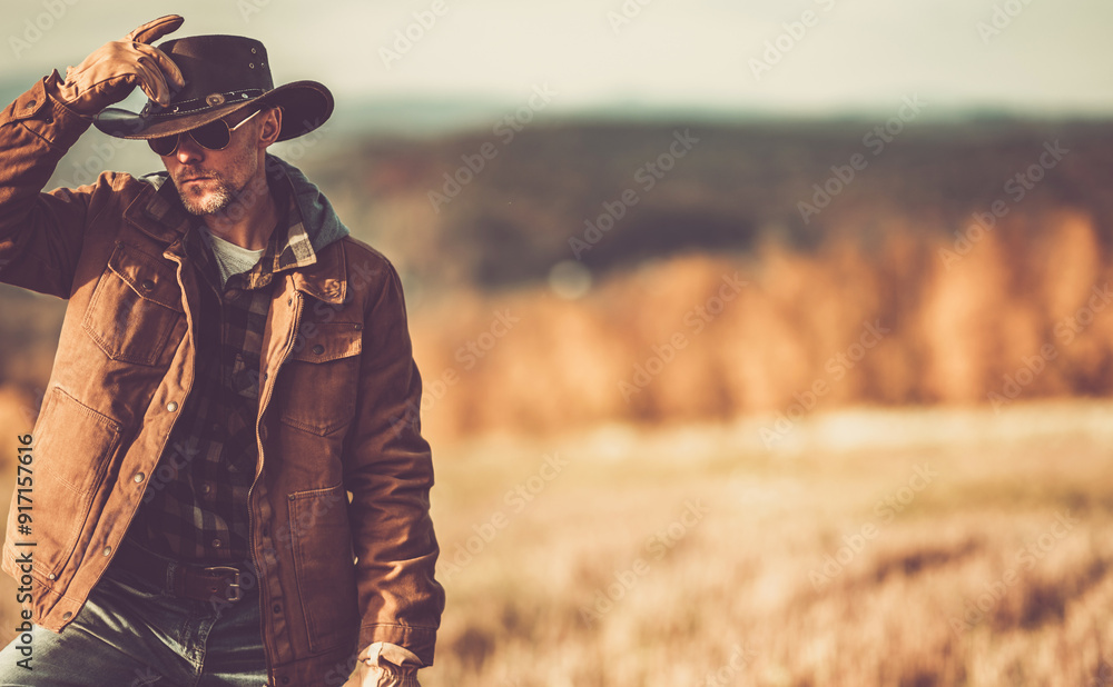 Fototapeta premium Man in a Cowboy Hat Poses Thoughtfully in a Golden Autumn Landscape During Sunset