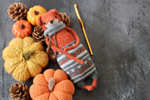 Halloween decoration with pumpkins, crocheted Fox toy and orange wool yarn on grey background with space for text. Handmade autumn gift. 