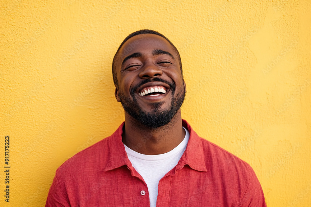 Close-Up Portrait of a Happy Black Man Laughing, Sunlight on His Face, Wearing a Red Shirt Over a White T-Shirt, with Yellow Wall Background Close-Up Portrait of a Happy Black Man Laughing, Sunlight on His Face, Wearing a Red Shirt Over a White T-Shirt, with Yellow Wall Background