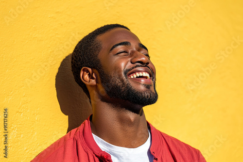 Black Man in Red Shirt and White T-Shirt, Laughing Joyfully on a Sunny Day, Close-Up Portrait with Sunlight and Yellow Wall Backdrop 