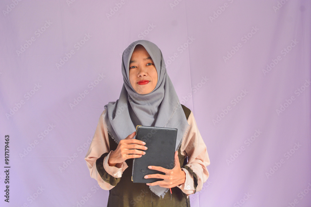Portrait of joyful smiling positive woman with dark wavy hair standing holding paper notebook and showing empty paper, copy space. Indoor studio shot isolated on background. Portrait of joyful smiling positive woman with dark wavy hair standing holding paper notebook and showing empty paper, copy space. Indoor studio shot isolated on background.
