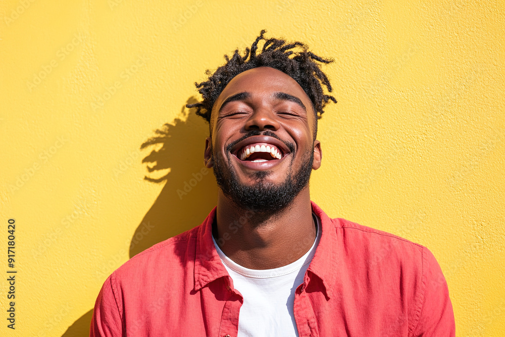 Fototapeta premium Black Man in Red Shirt and White T-Shirt, Laughing Joyfully on a Sunny Day, Close-Up Portrait with Sunlight and Yellow Wall Backdrop 