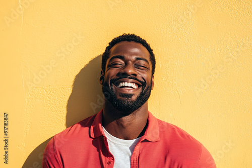 High-Quality Headshot of a Laughing Black Man, Sunlit and Smiling, Wearing a Red Shirt and White T-Shirt, Set Against a Yellow Wall