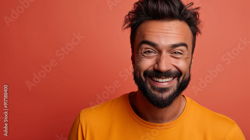 A smiling man with a beard radiates happiness in front of a bright orange backdrop, showcasing a lighthearted and joyful moment