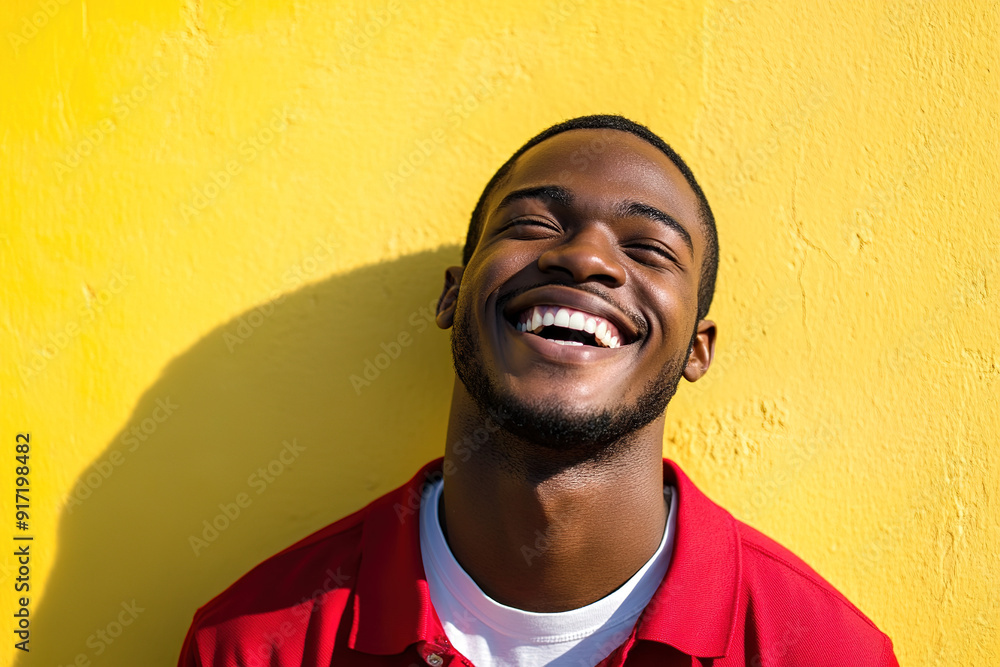 Bright and Cheerful Headshot of a Black Man Wearing a Red Shirt and White T-Shirt, Smiling on a Sunny Day with a Yellow Wall Behind Bright and Cheerful Headshot of a Black Man Wearing a Red Shirt and White T-Shirt, Smiling on a Sunny Day with a Yellow Wall Behind