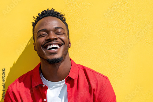 Bright and Cheerful Headshot of a Black Man Wearing a Red Shirt and White T-Shirt, Smiling on a Sunny Day with a Yellow Wall Behind