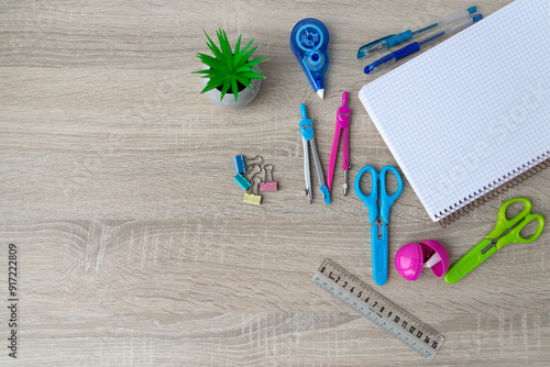 Assorted stationery items arranged on a wooden surface. A variety of colorful stationery items, including scissors, pens, a ruler, a notebook, and a plant, are neatly arranged on a wooden surface. Top photo