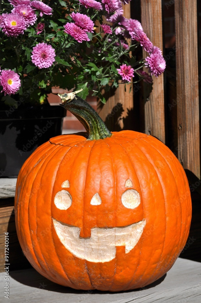 Obraz premium Close up of happy hand carved orange pumpkin and purple flowers on wooden stairs.