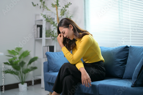 Woman in Yellow Sweater Sitting on Blue Sofa in Modern Living Room with Plants and Shelves