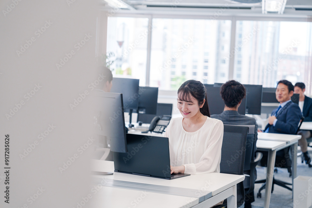 オフィスで笑顔でデスクワークをする若い女性 オフィスで笑顔でデスクワークをする若い女性