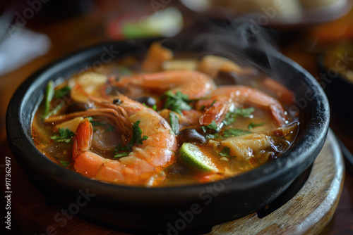 Savory and Aromatic Tom Yum Goong with Fresh Prawns Steaming Hot in a Black Bowl, Garnished with Herbs. Perfect for Spicy Food Lovers! photo