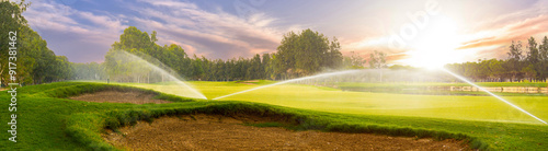 Golf course sprinklers in action at sunset. Concept of maintaining a lush green fairway