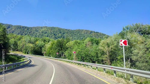 Scenic drive through the forest, view from the windshield of the car. Scenic road framed by beautiful green trees, winding among the mountains, view through the windshield of the car.
