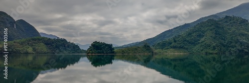 Tranquil lake surrounded by lush green mountains reflecting in the water under a cloudy sky, perfect for nature retreats